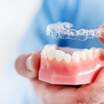Dentist holding clear aligners and a mouth mold 