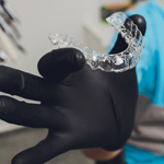 Gloved hand holding a clear aligner 