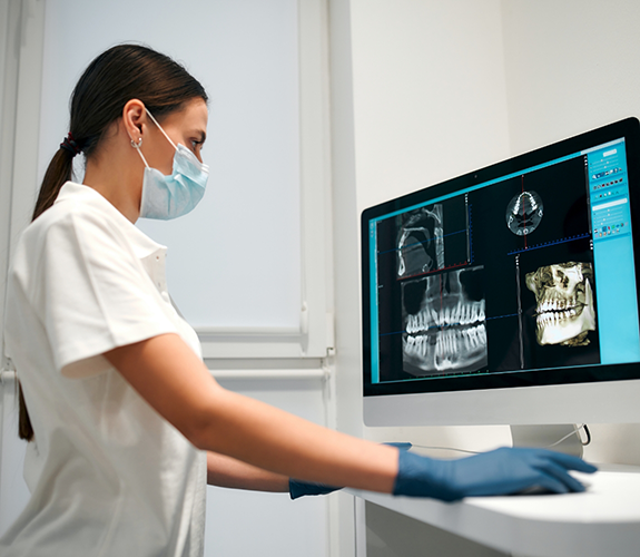 Female dentist with mask looking at digital X rays on computer monitor