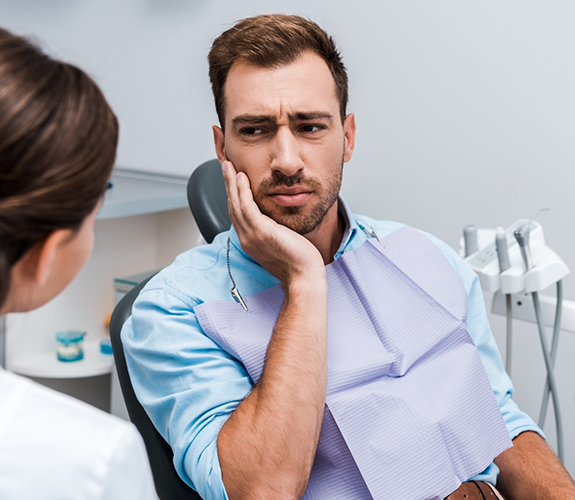 Man sitting in dental chair rubbing his jaw in pain