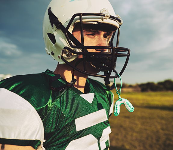 Young boy with football helmet with mouthguard dangling off