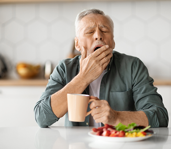 Man holding cup of coffee yawning