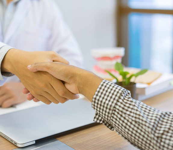 Dentist and patient shaking hands over desk